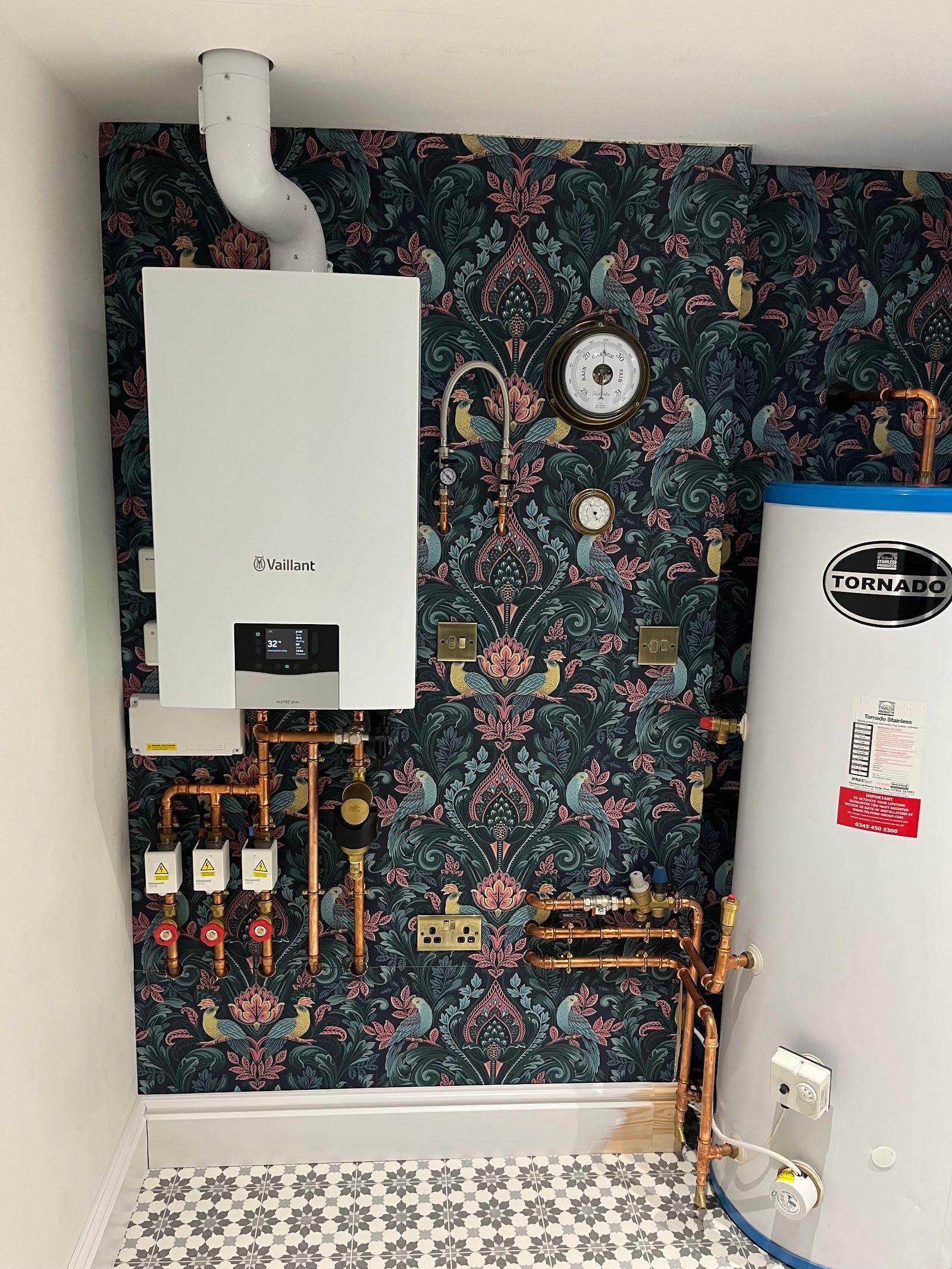 A Vaillant boiler and hot water cylinder fitted in a utility room with patterned wallpaper