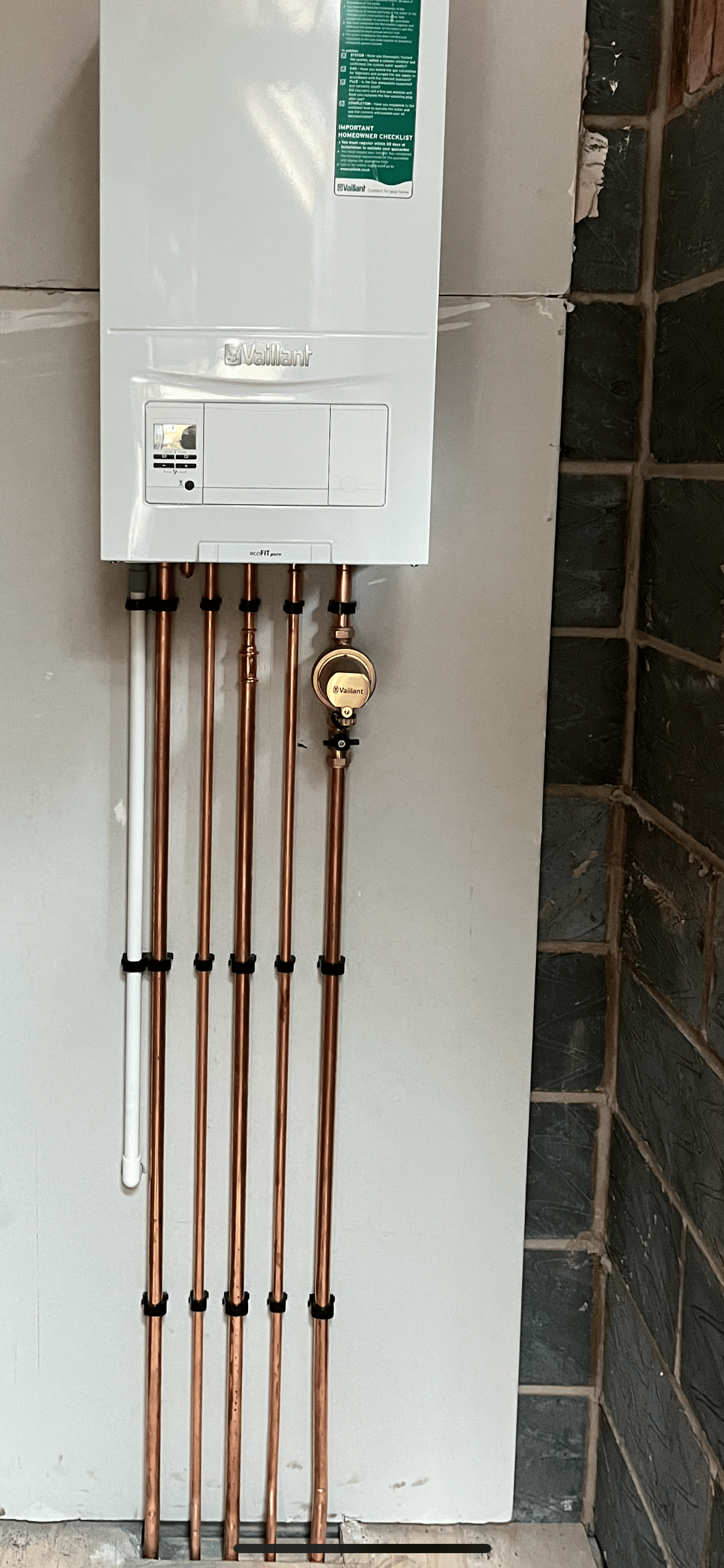 A boiler with five copper pipe drops and a gas valve, against a tiled wall